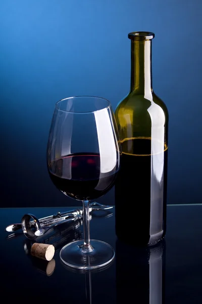 Een glas rode wijn met flessen op een blauwe achtergrond — Stockfoto