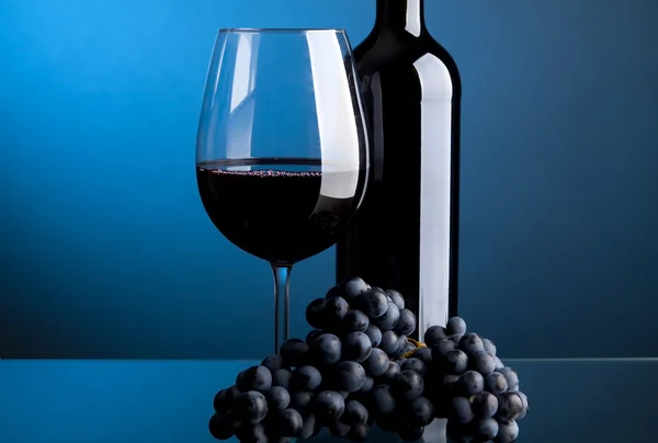 Un pahar de vin roșu cu sticle pe fundal albastru — Fotografie, imagine de stoc