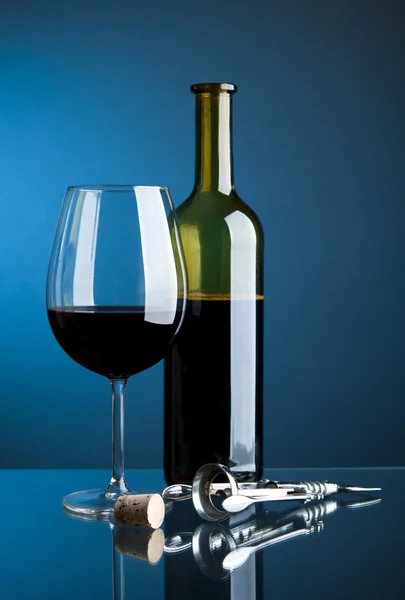 Een glas rode wijn met flessen op een blauwe achtergrond — Stockfoto
