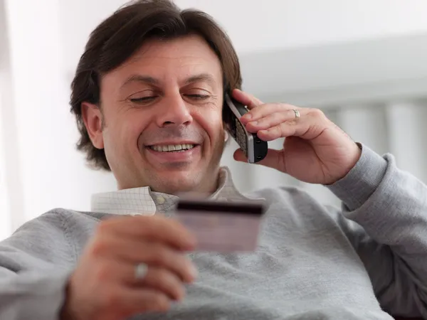 Взрослый мужчина делает покупки из дома с телефоном и кредитной картой — стоковое фото