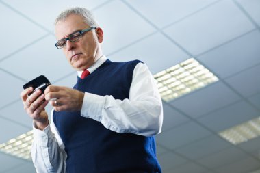 Mature businessman reading e-mails on cellphone clipart