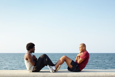 Two men exercising abs near the sea clipart