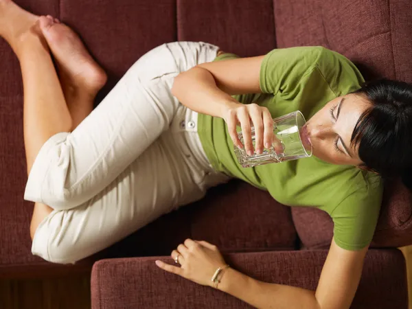 Женщина пьет воду на диване — стоковое фото