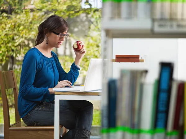 Девушка держит яблоко в библиотеке — стоковое фото