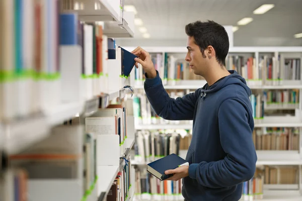 Homem escolhendo livro na biblioteca — Fotografia de Stock