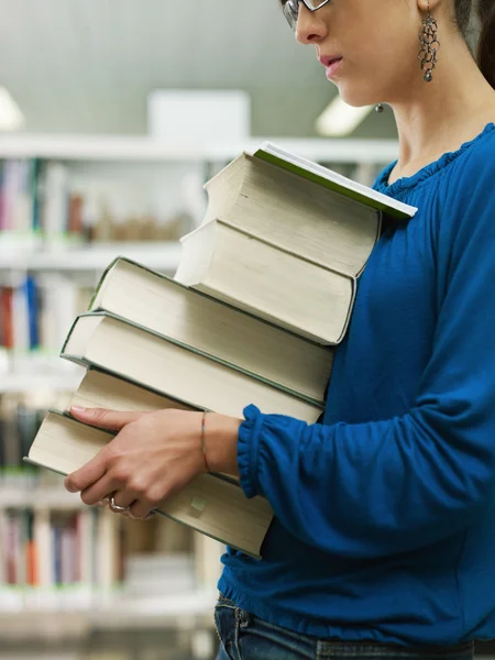 Женщина с грудой книг в библиотеке — стоковое фото
