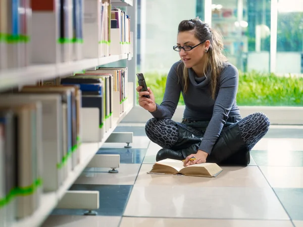 Dívka textových zpráv s telefonem v knihovně — Stock fotografie