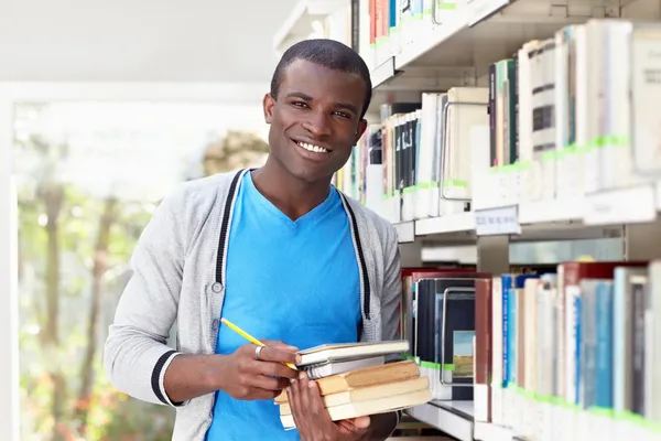 Молодой африканский мужчина улыбается в библиотеке — стоковое фото
