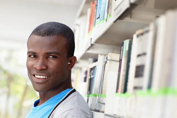 Mladý africký muž usmívající se v knihovně — Stock fotografie