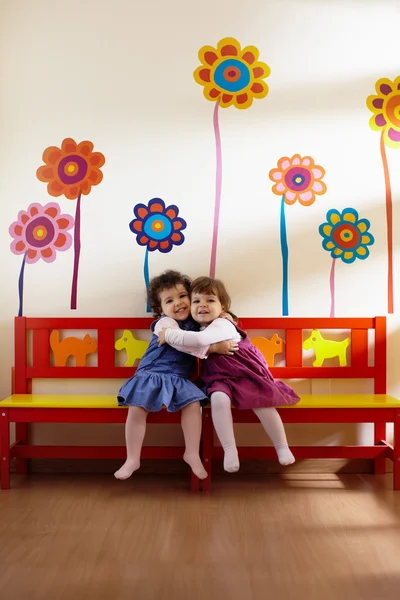 Zwei kleine Mädchen lächeln und umarmen sich in der Schule Stockbild
