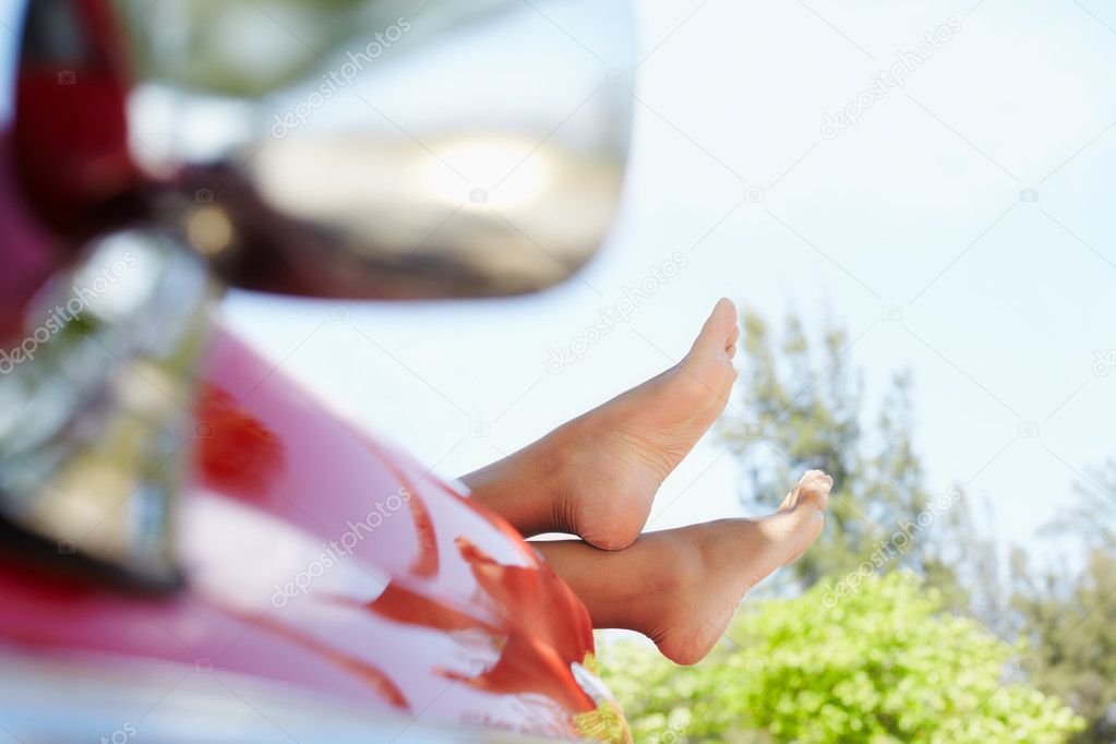 Woman lying in cabriolet car with feet out of window