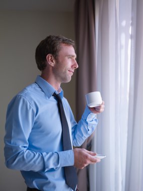 Businessman drinking coffee and looking out of window clipart