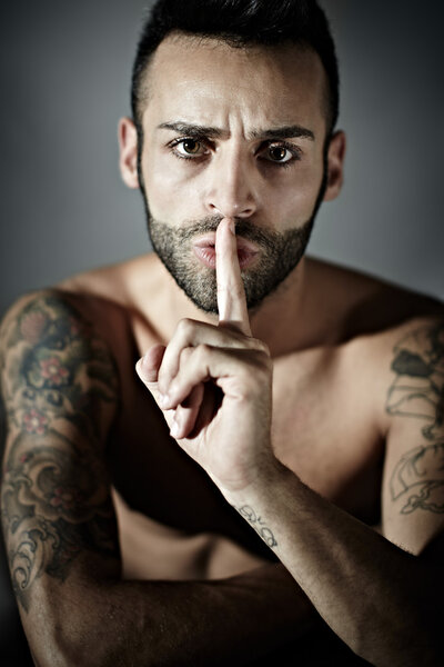 Tattooed man with finger on mouth