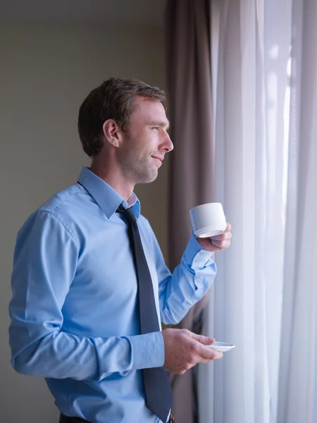 Affärsman dricka kaffe och titta ut genom fönster — Stockfoto