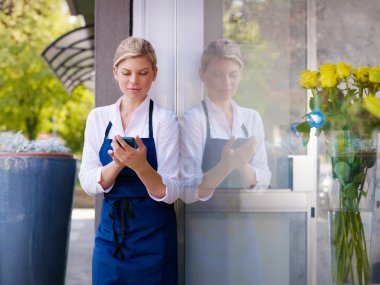 Young woman working as florist in shop and text messaging clipart