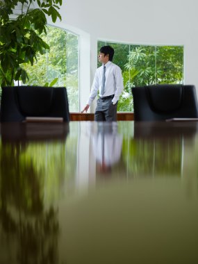 Businessman contemplating out of window in meeting room clipart