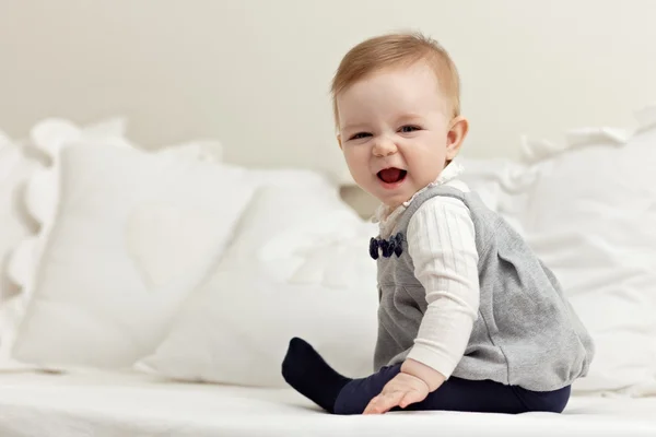 Kleines Mädchen sitzt auf dem Bett und lacht — Stockfoto
