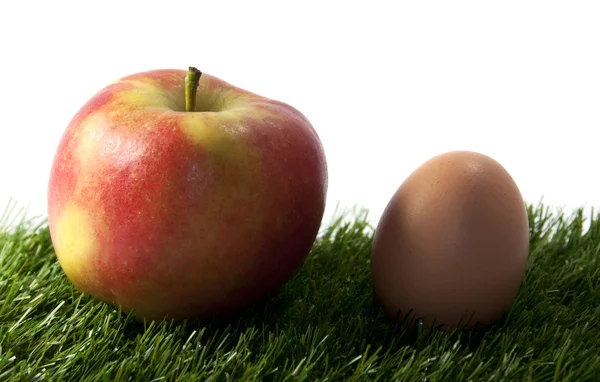 Яблоко и яйцо на зеленой траве — стоковое фото