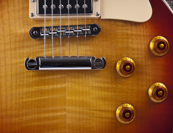 Close up shot of a sunburst electric guitar showing pickup, strings, bridge and volume controls