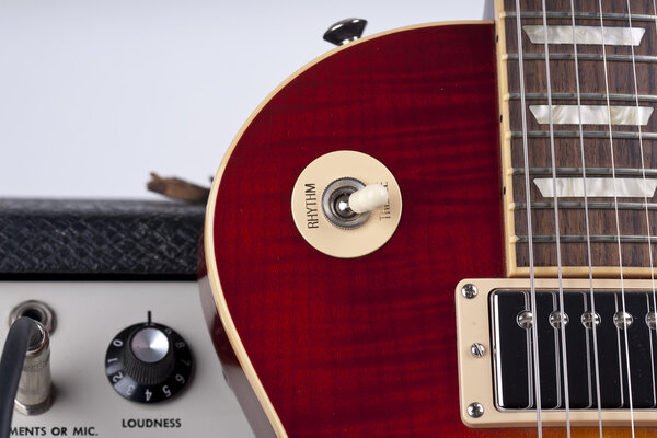 Close up of a beautiful electric guitar leaning against a vintage amplifier with black knobs