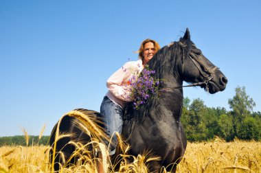 Beautiful smiling woman rides pretty black horse in field clipart