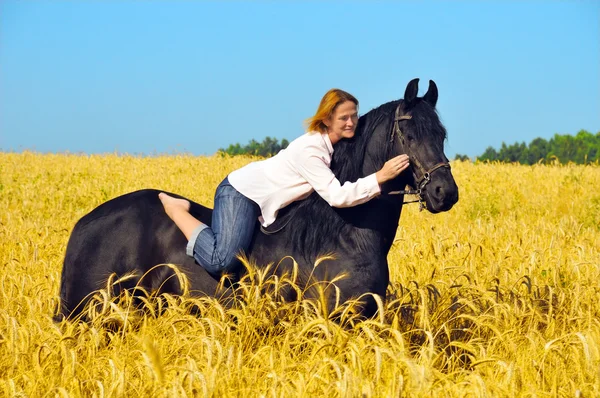 Beautiful woman rides and pets horse in field — Zdjęcie stockowe
