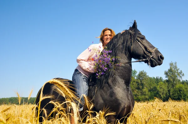 Vackra leende kvinna Rider ganska svart häst i fältet — Stockfoto