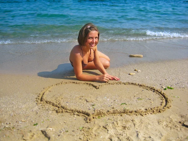 Beautiful girl drawing heart on sand — Stock Photo, Image