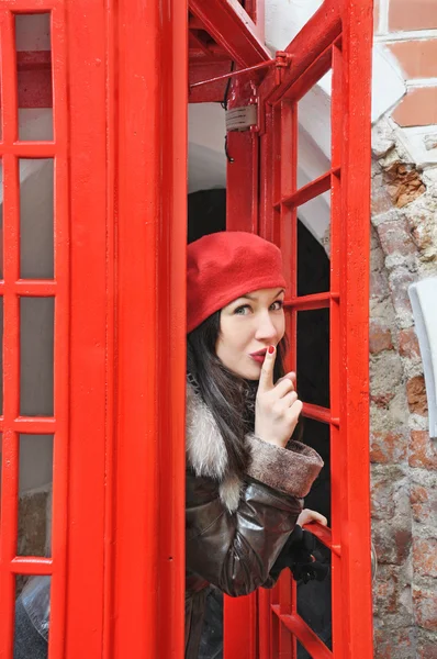 红色帽子的年轻女人看从 phonebox — 图库照片