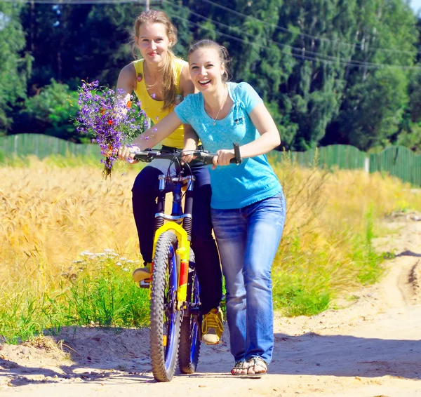 Hermosas chicas sonrientes caminan con bicicleta en el camino del pueblo —  Fotos de Stock
