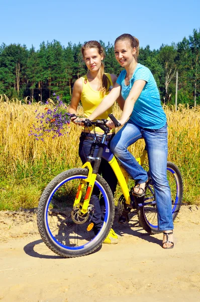 Hermosas chicas sonrientes montar en bicicleta en el camino del pueblo —  Fotos de Stock