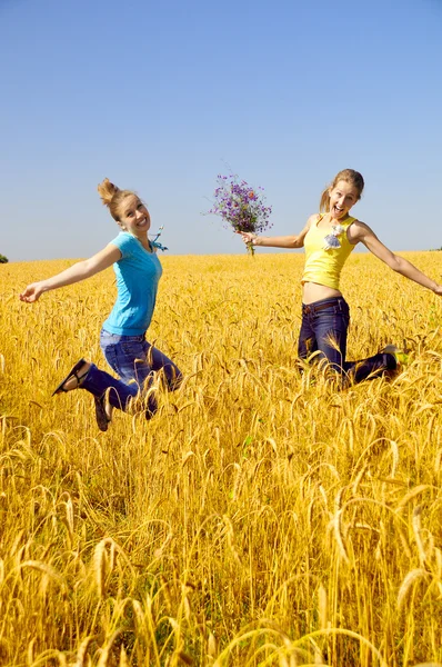 Two beautiful girls jumps in golden field — Stock Photo, Image