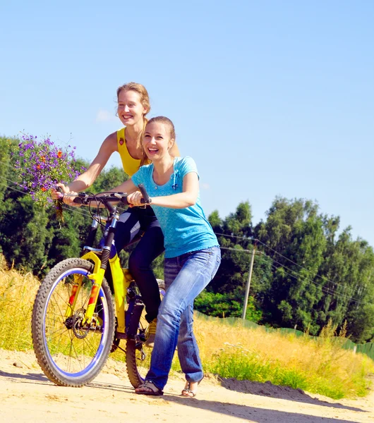 Hermosas chicas sonrientes suben la colina con bicicleta en el pueblo —  Fotos de Stock