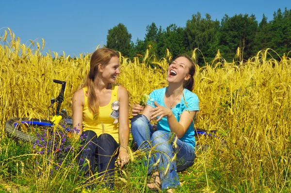 Dos chicas hermosas riendo descansan en el campo de verano dorado —  Fotos de Stock