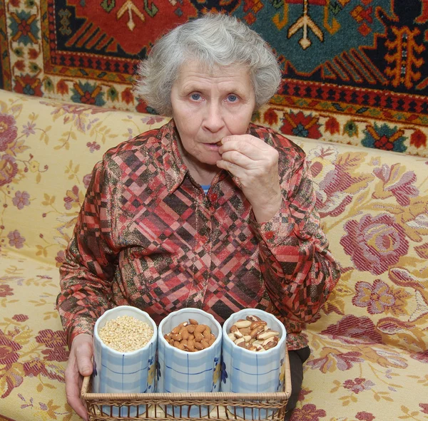 Εβδομήντα έτος ηλικιωμένη γυναίκα κάθεται στον καναπέ και ρωγμές καρύδια — Φωτογραφία Αρχείου