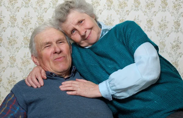 Glücklich lächelndes altes Paar, das zusammen in der Umarmung des anderen sitzt — Stockfoto