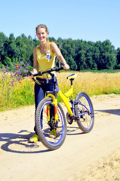 Hermosa chica sonriente camina con bicicleta en el camino del pueblo —  Fotos de Stock