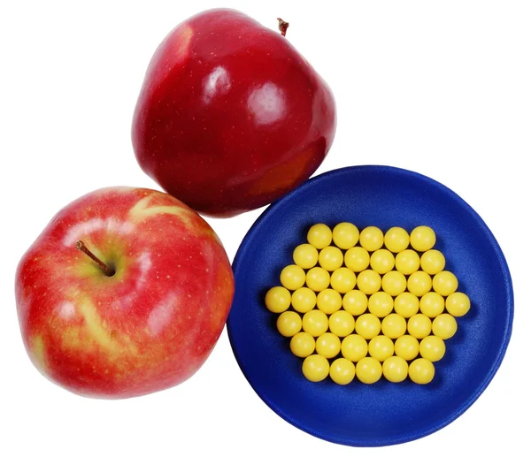 Azul plateful de gotas amarelas vitamina e maçãs vermelhas acima deles — Fotografia de Stock