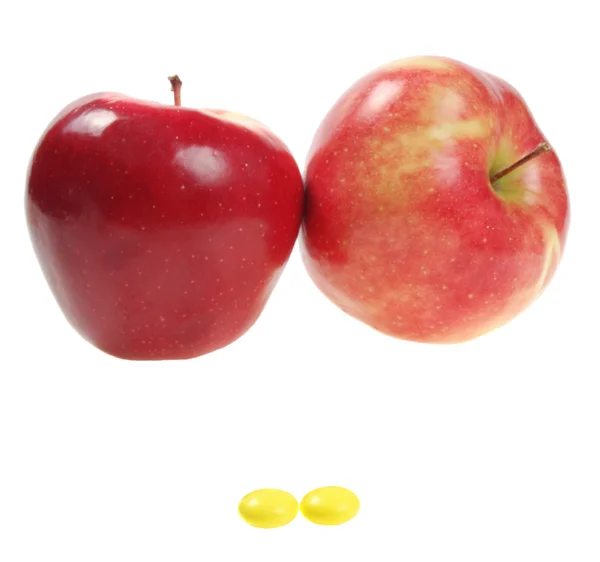 Две желтые таблетки на фоне двух красных яблок — стоковое фото