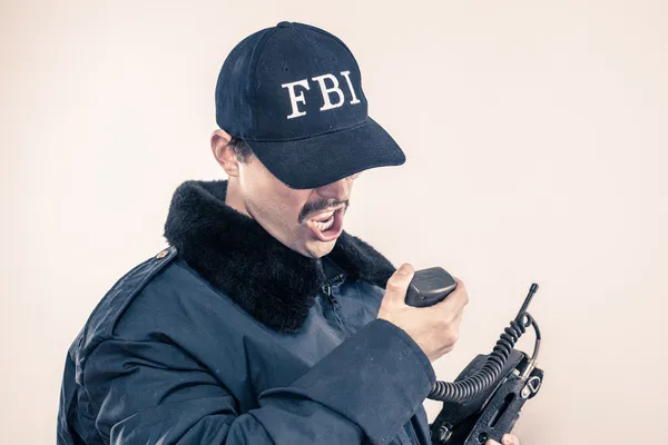 Furious FBI man bearing teeth under cap, blue jacket on vintage radio Stock Picture