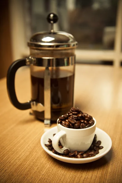 Маленькая чашка кофе в зернах и пресса — стоковое фото