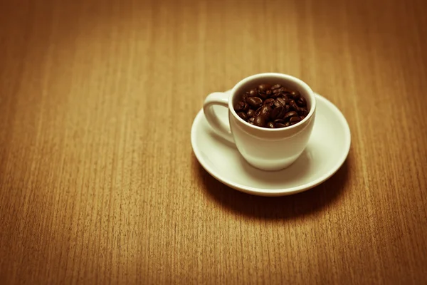 Weißer Kaffeebecher auf weißem Teller mit Bohnen gefüllt — Stockfoto