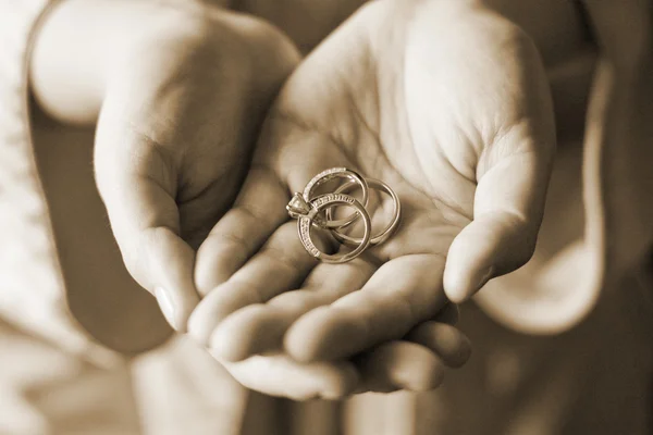 Sephia in stile primo piano Visualizza due mani che tengono tre anelli di nozze — Foto Stock