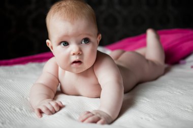 Infant lying on a white rug, and surprised looks away clipart