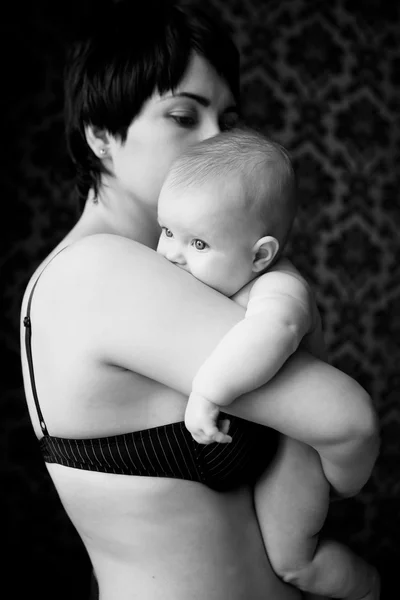Yan ilgiyle izleyen bir tombul bebek tutan anne — Stok fotoğraf