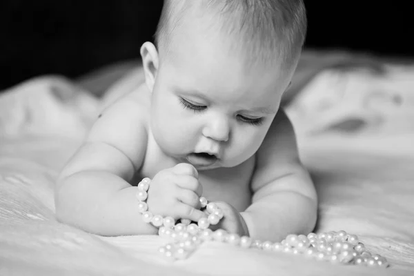 Infant girl plays with enthusiasm pearl beads lying on tummy — Stock Photo, Image