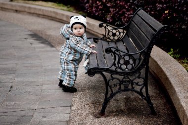 Cute little boy is holding on to the bench clipart