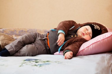 Cute little boy sleeps in the clothes on a bed clipart