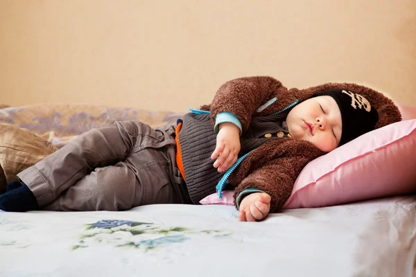 Bonito menino dorme na roupa em uma cama — Fotografia de Stock