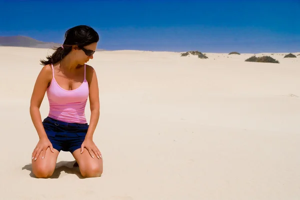 Stock image profile-only girl kneeling on the sand with blue sky